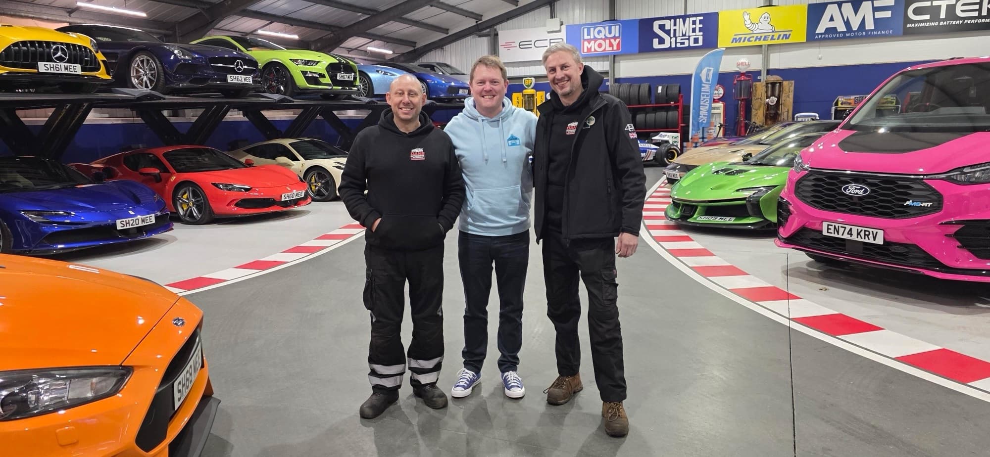 At a supercar garage, with a Shmee150 banner visible behind